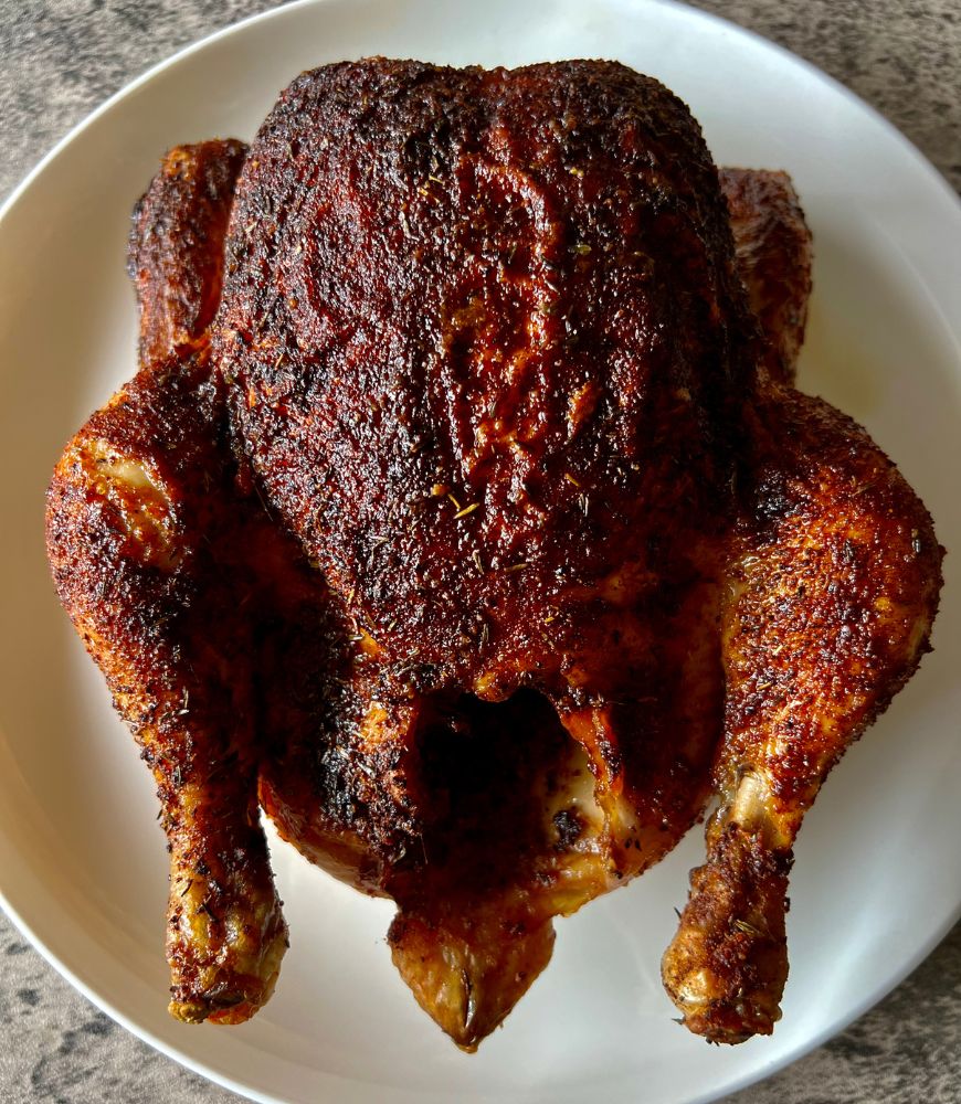 roasted whole chicken in spice rub on white plate, close up image