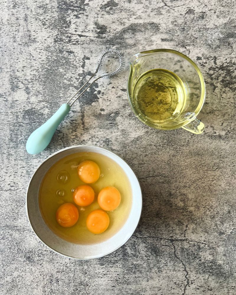 eggs in white bowl, whisk and jug of oil