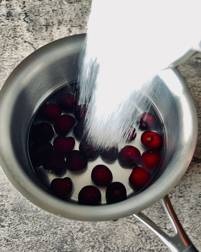 adding sugar to cherries in a pan