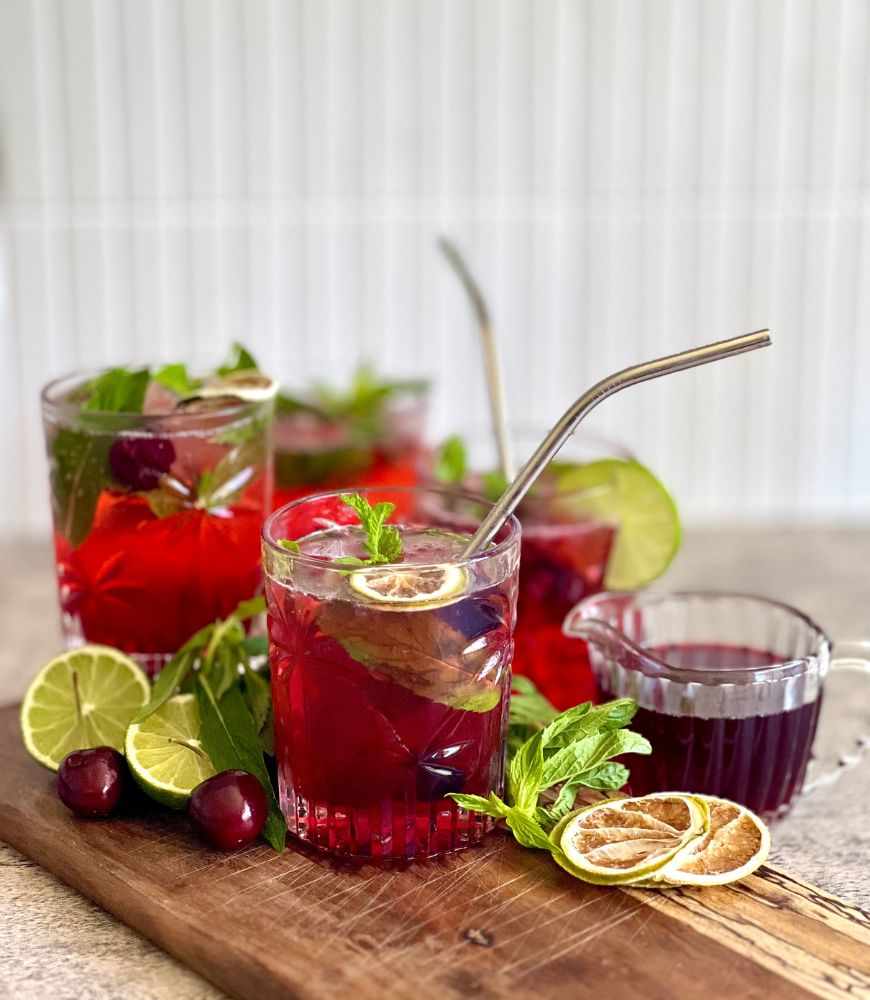 cherry mojitos in glasses on wood board with lime mint and cherries