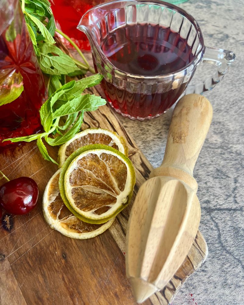 cherry syrup in glass jug, wooden juicer and limes