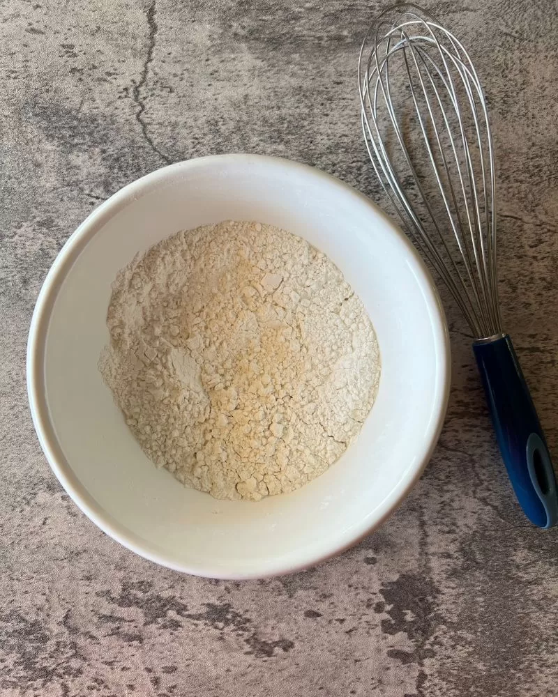white bowl with flour in it. Whisk next to it