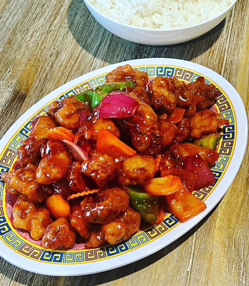 sweet and sour pork on Chinese plate with bowl of rice in white bowl