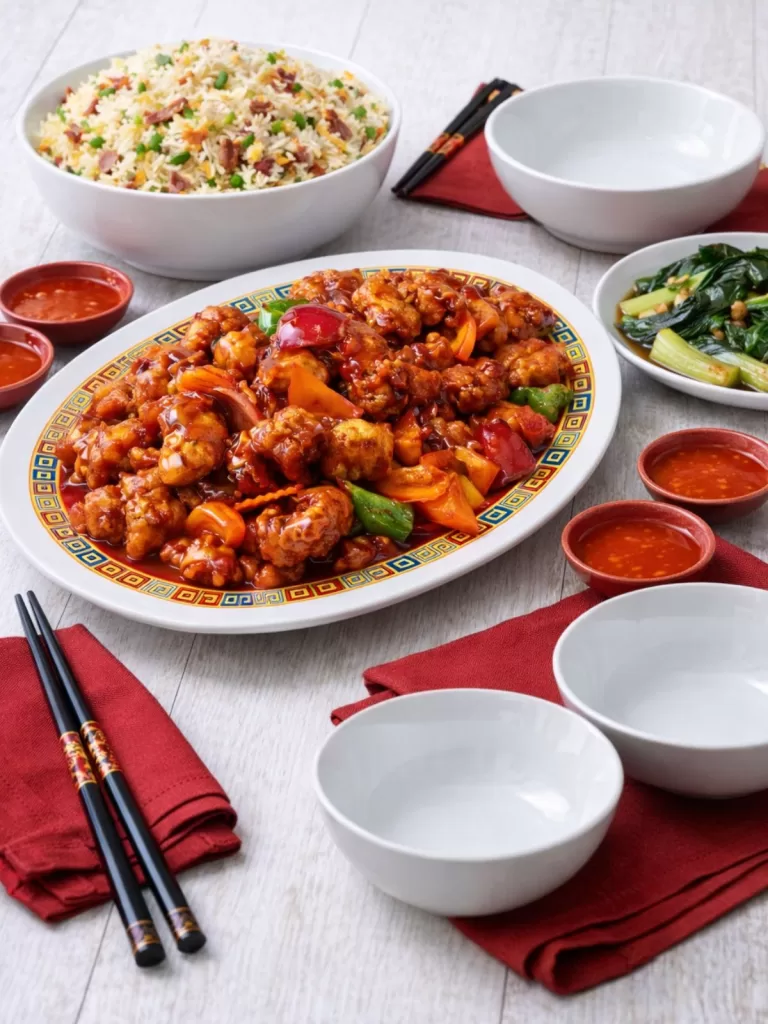 table setting of sweet and sour pork getting ready to be eaten with fried rice and asian greens in oyster suace.
