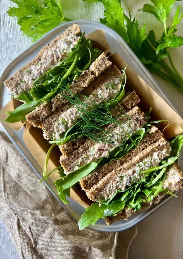 tuna sandwiches sitting in baking dish on white background with celery sprigs around it and beige napkin