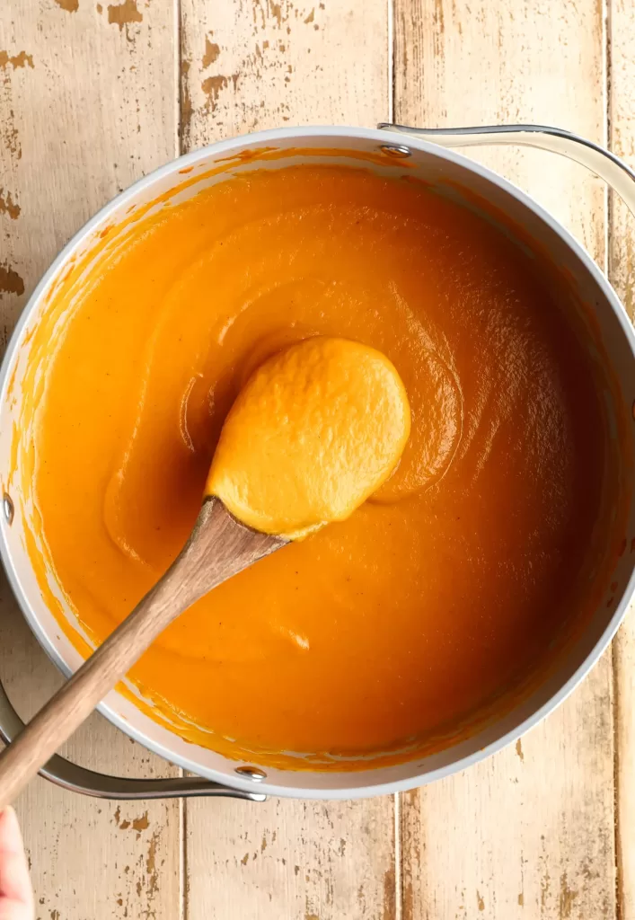 pureed carrot soup in white saucepan and wooden spoon in it