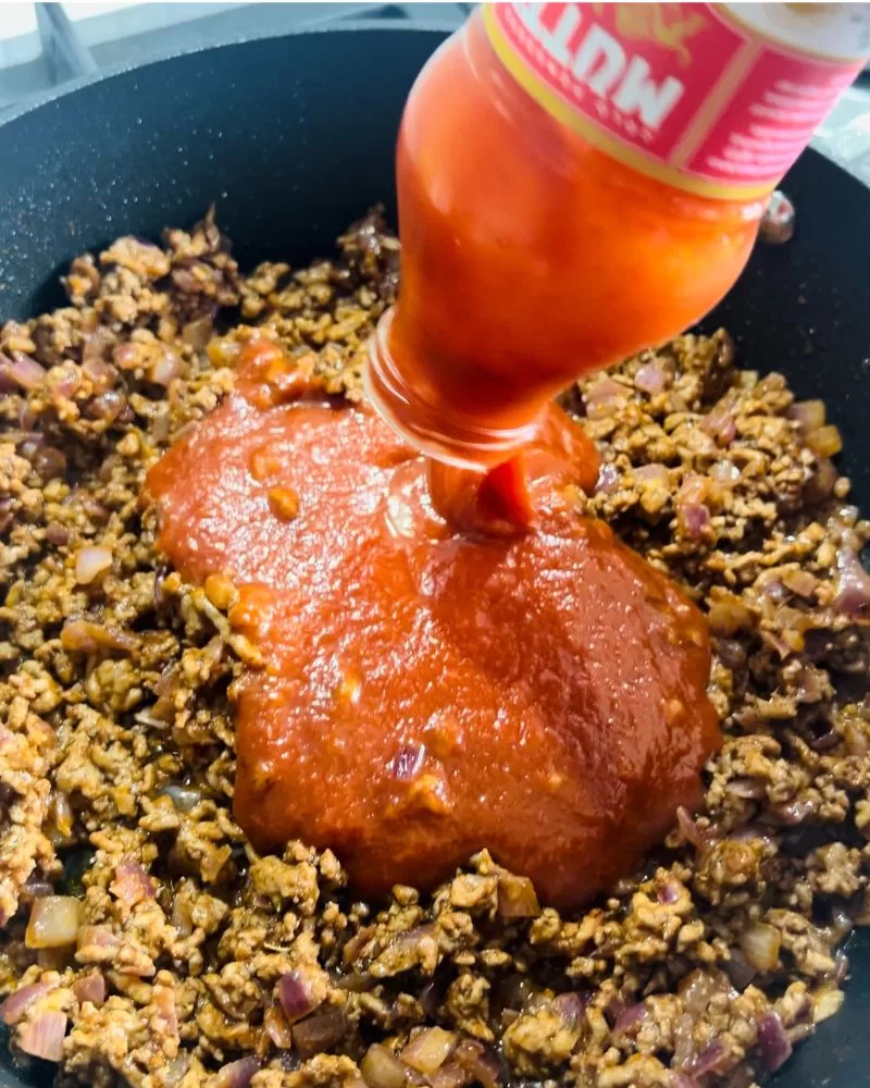 pouring a bottle of pasta sauce into frying pan