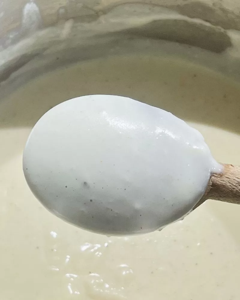 close up of bechamel sauce on the back of a wooden spoon