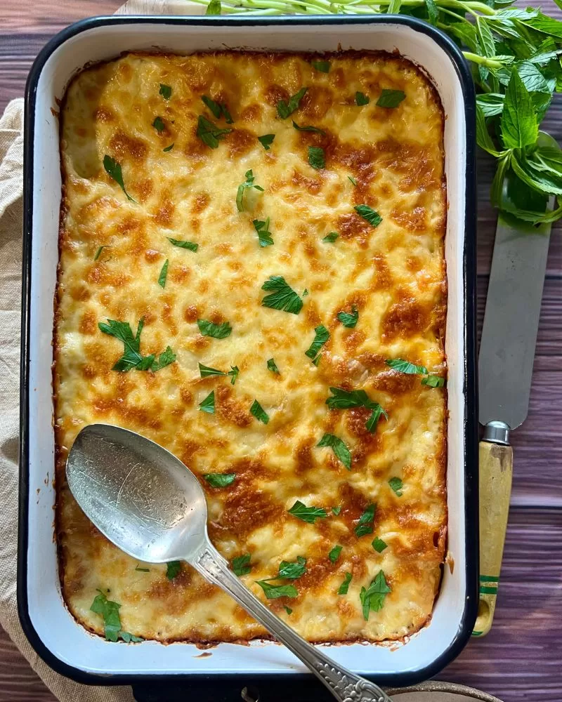 cheesy pasta bake in a dish with spoon and herbs around it