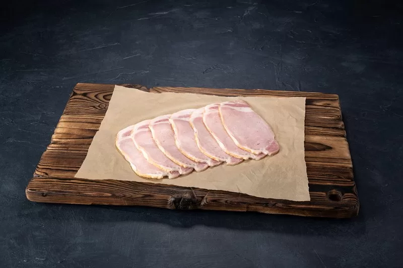 bacon fanned out on baking paper on wood board. Dark background