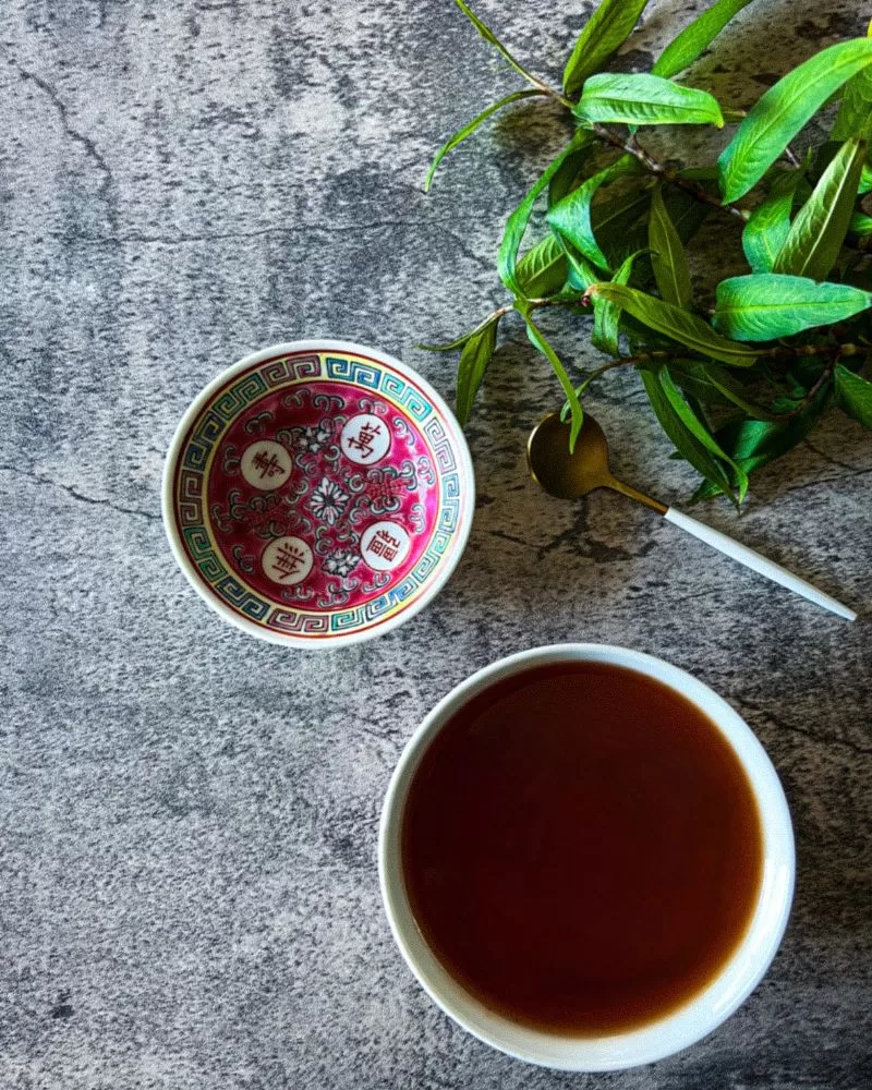 sweet and sour sauce in white bowl. Small Chinese print bowl to the left and some herbs and a white and gold teaspoon above it