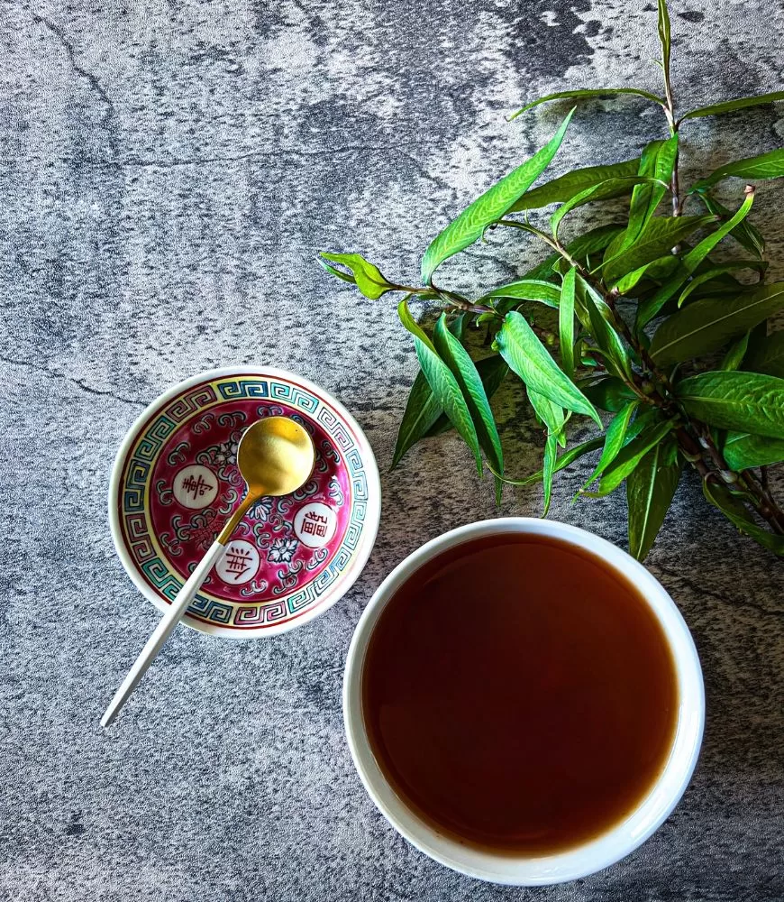 Chinese Sweet & Sour Sauce in white bowl on marble background. Small Chinese bowl with white and gold spoon and bunch of herbs next to it