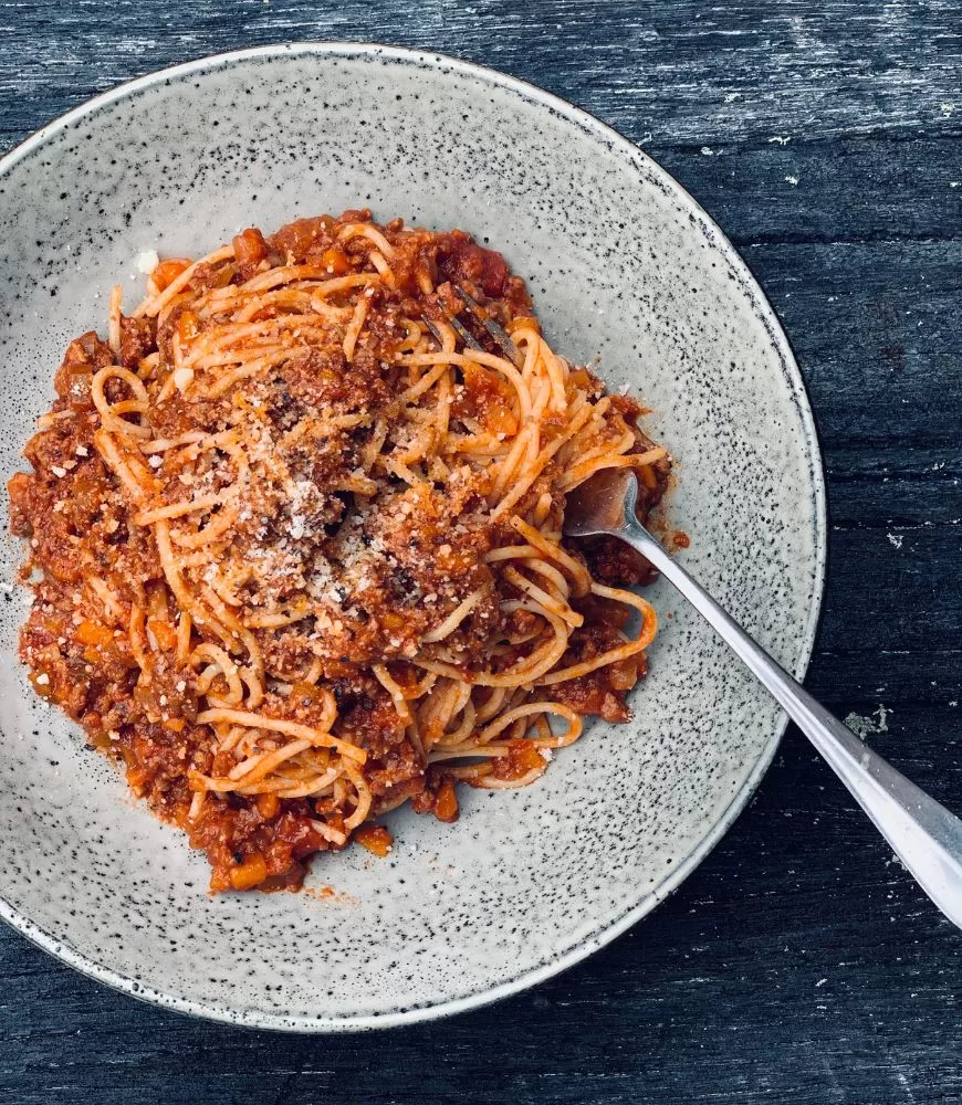 spaghetti bolognese in speckled beige bowl with fork on wooden background