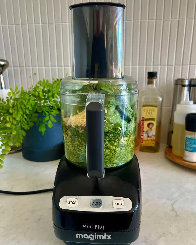 food processor on kitchen bench with pesto ingredients in it