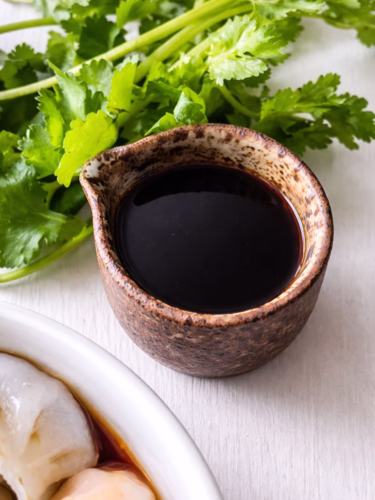 jug of dumpling sauce on a white background with a bunch of coriander.