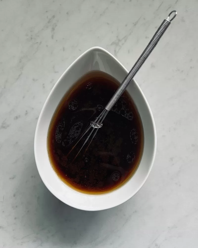 dumpling sauce in a white dish with small metal whisk in it