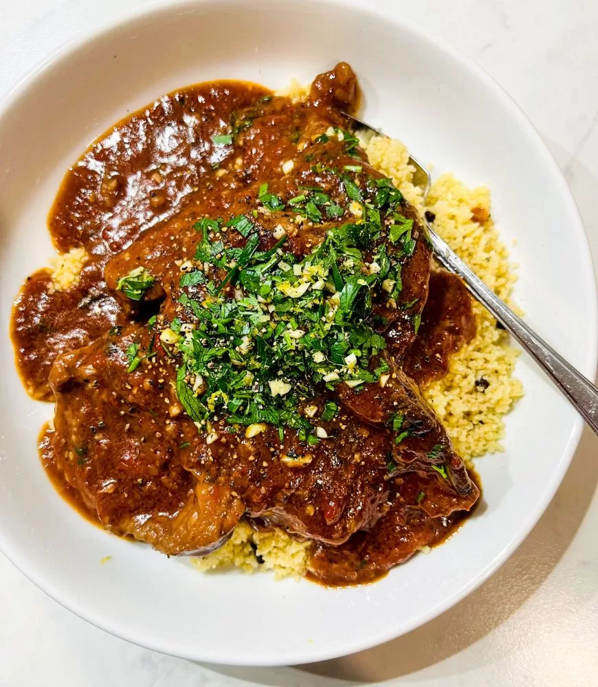 slow simmered lamb in tomato, garlic and red wine in a white bowl with couscous