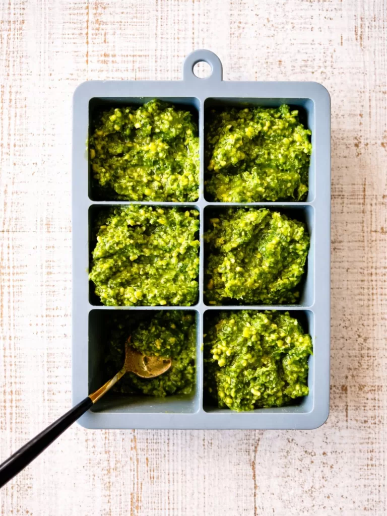 thai basil pesto in ice cubes trays with a spoon. white timber background.