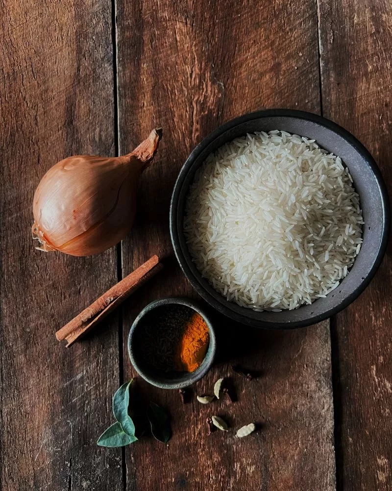 wood board with onion, spices and bowl of uncooked rice