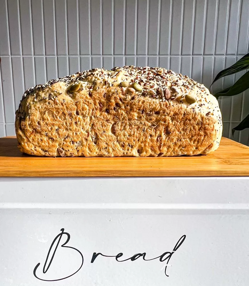 Five Grain Bread Loaf sitting on a wooden board on bread tin