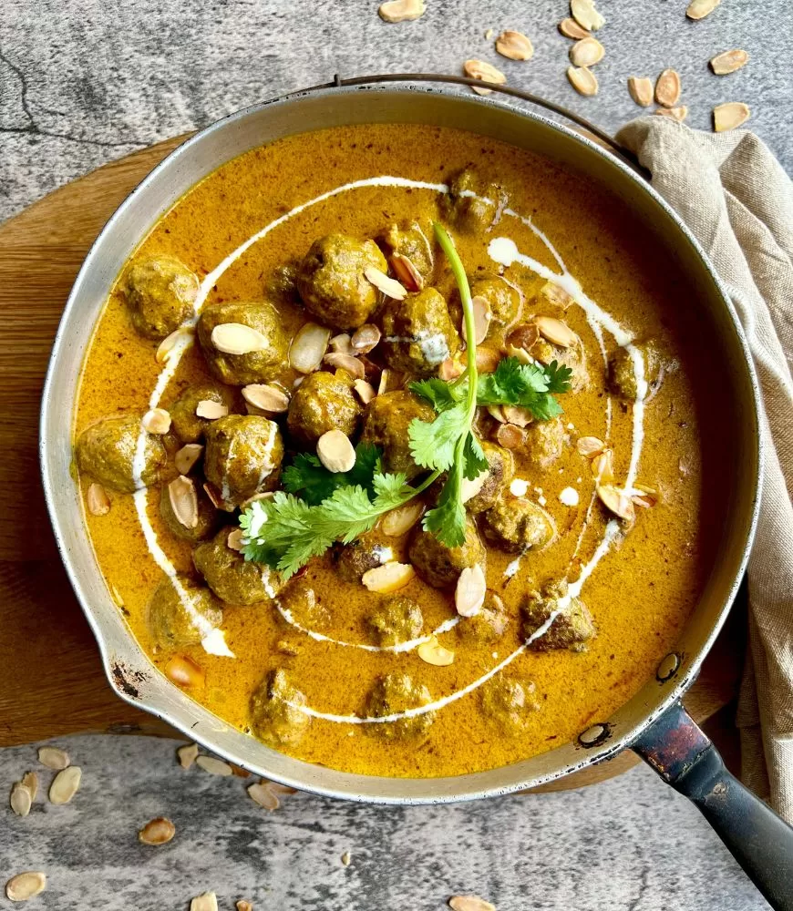 lamb korma meatballs in frying pan topped with almonds, cream and coriander. Grey and wood background