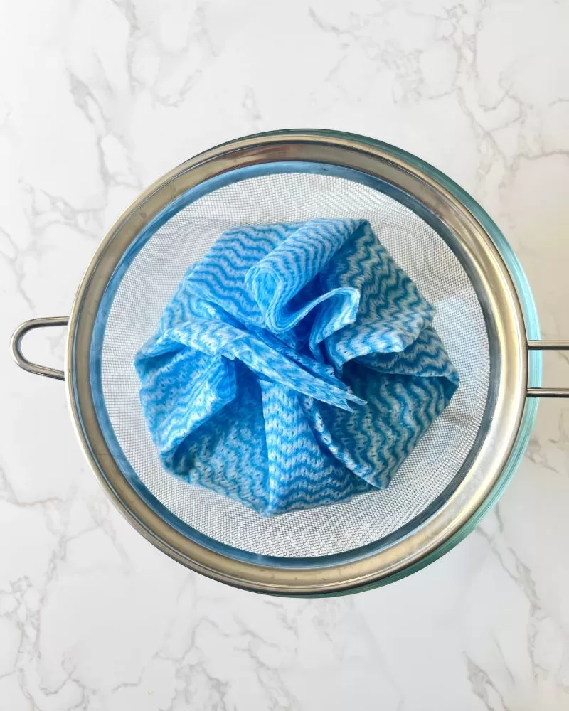 blue cloth in sieve over a glass bowl