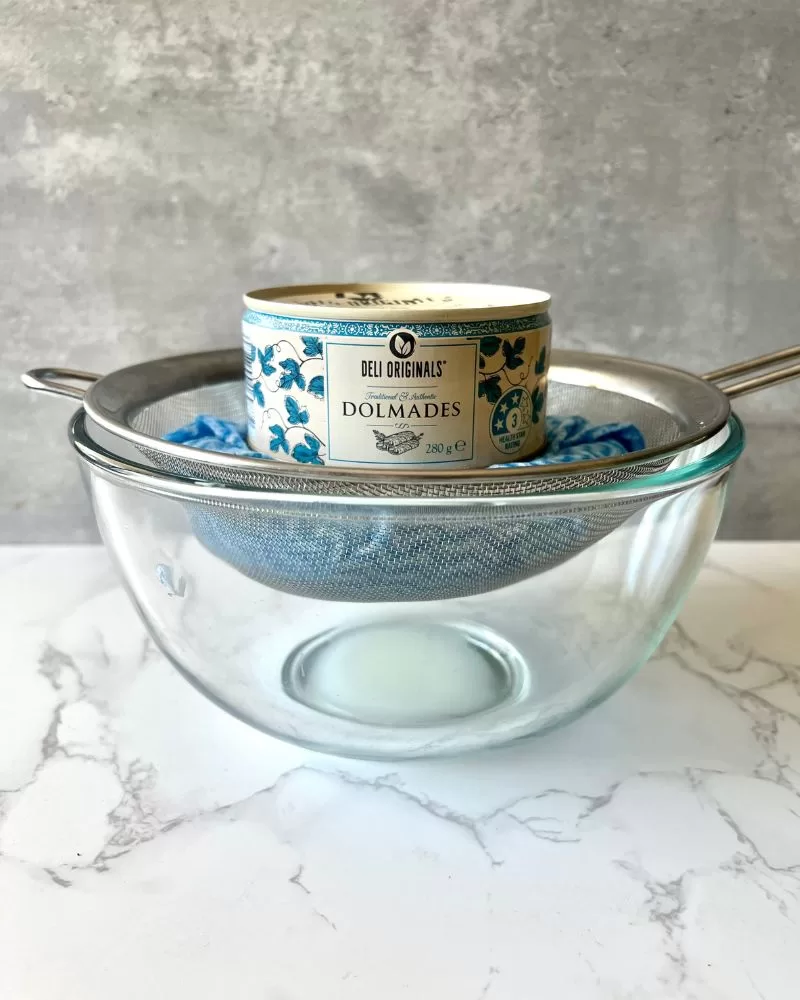 glass bowl with sieve, blue cloth and can of food on top weighing it down