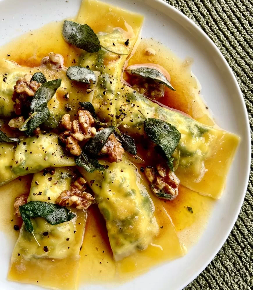 ravioli on white plate topped with butter sauce, walnuts and sage