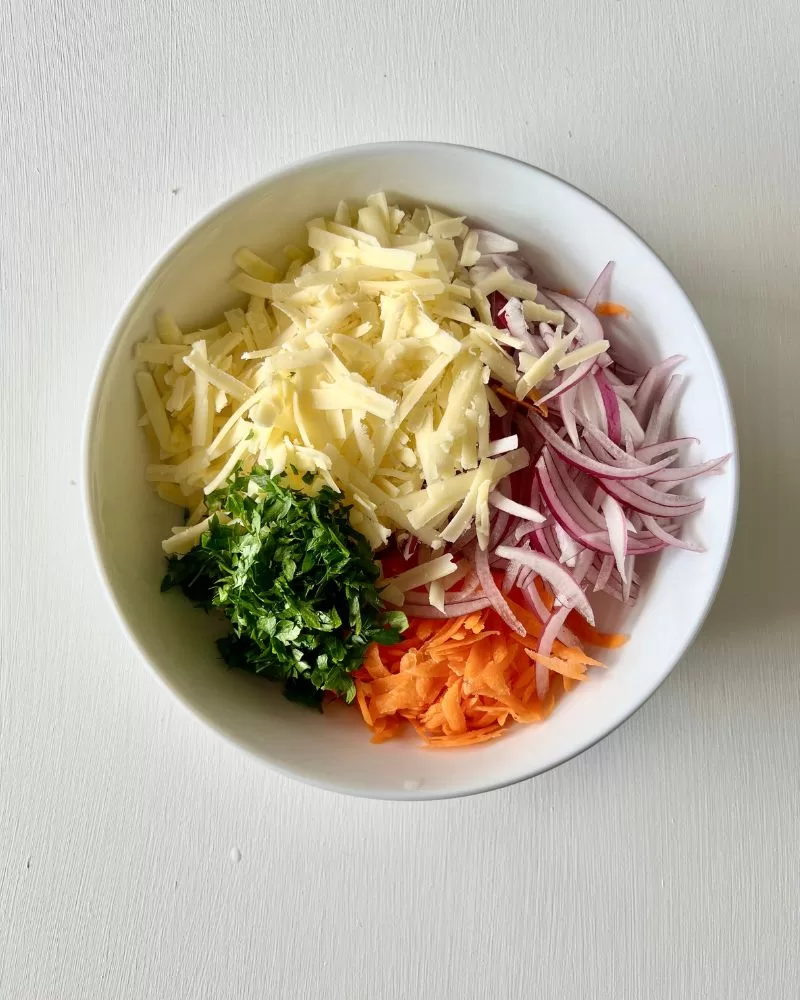 grated carrot, oinon, cheese, parsley in white bowl
