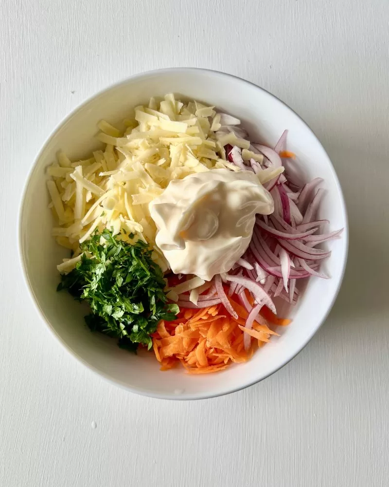 grated carrot, onion, cheese, parsley and mayonnaise in white bowl
