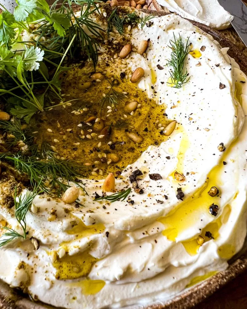close up of labneh dip with olive oil, herbs, za`atar, pine nuts and pepper