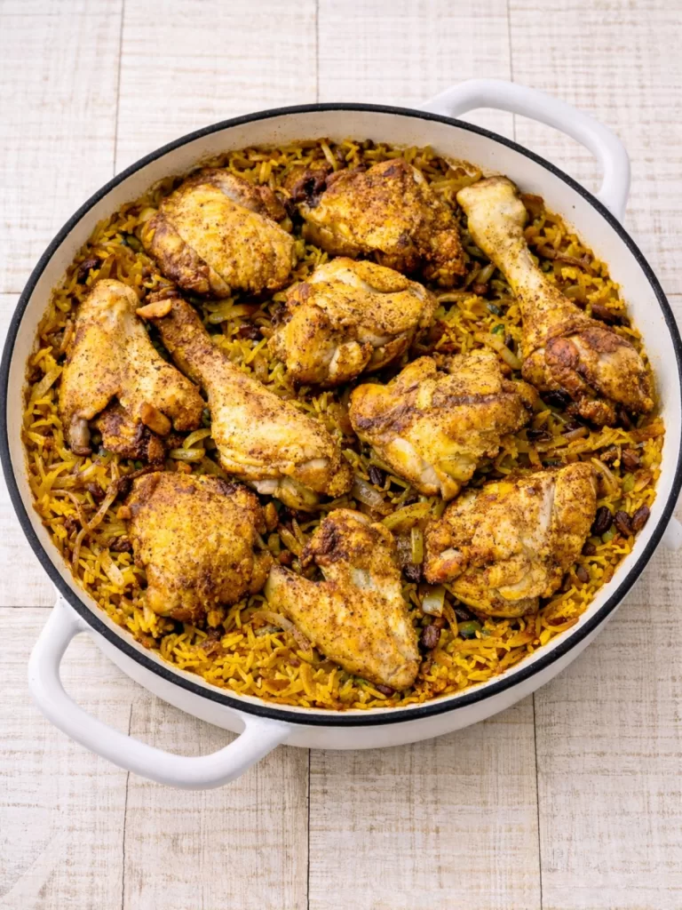 Middle Eastern chicken and rice in a white pan, with golden spiced chicken pieces over fragrant yellow rice on a white timber background.