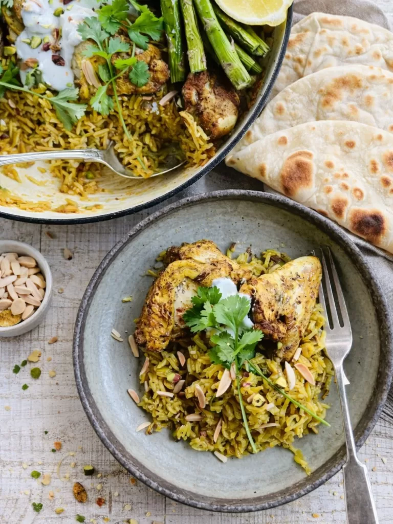 Chicken and rice served in a bowl, topped with spiced chicken, herbs, yogurt sauce and toasted nuts, with flatbread on the side.