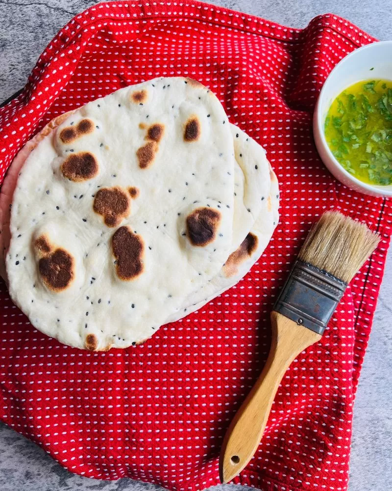 naan bread on tea towel with pastry brush and garlic butter