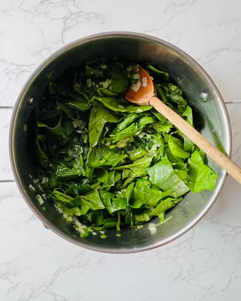 spinach leaves wilting in a saucepan with a wooden spoon in it.