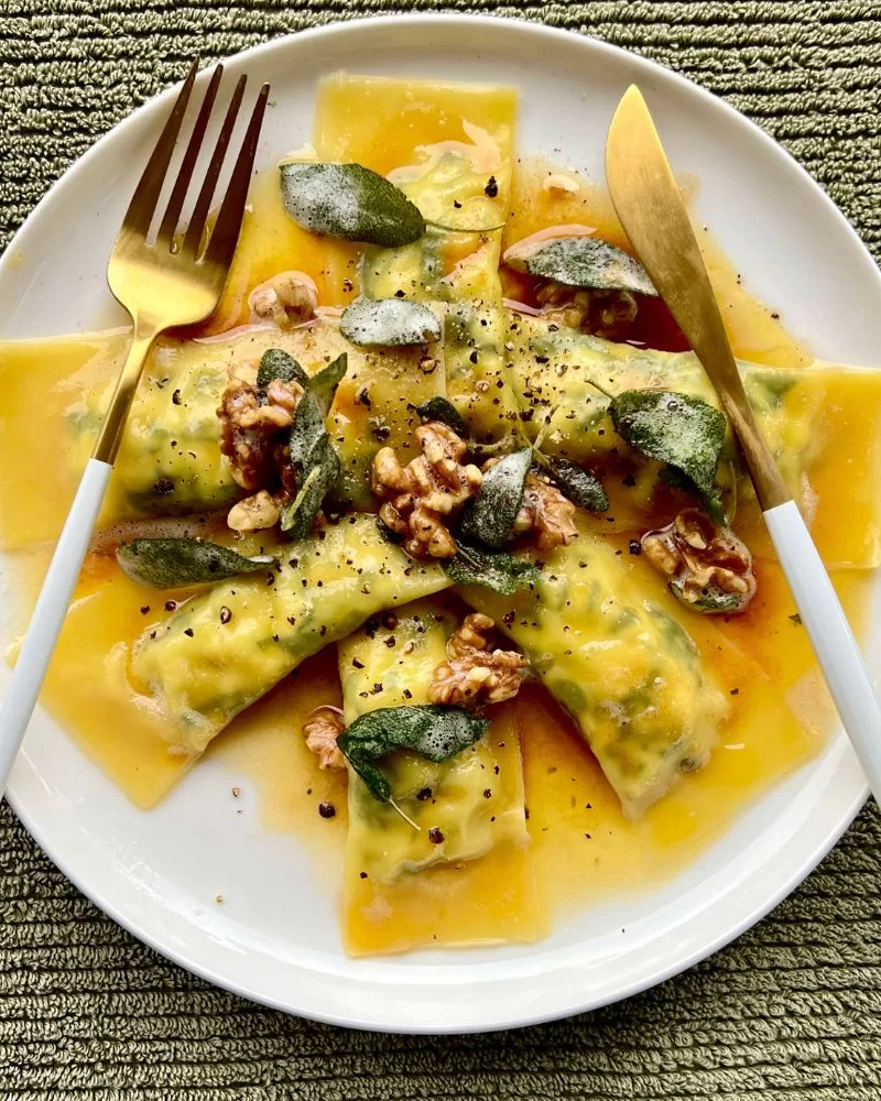 spinach and ricotta ravioli on plate with knife and fork. Green background