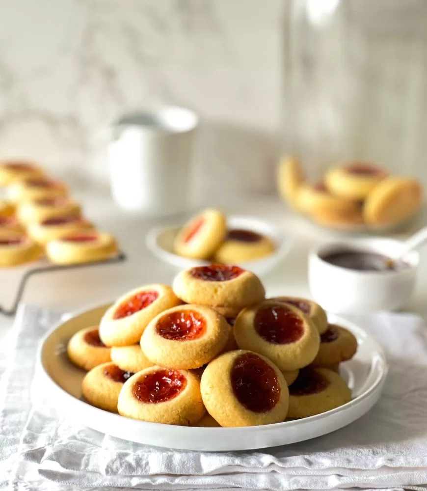 Mini Jam Drop  Biscuits piled up on a  white plate sitting on white cloth napkins with more in the background