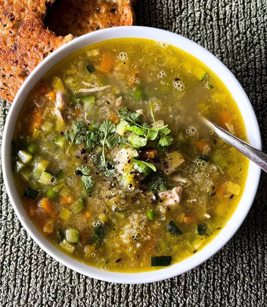 chicken & vegetable soup with quinoa in white bowl, silver spoon on green background. Toast to the side