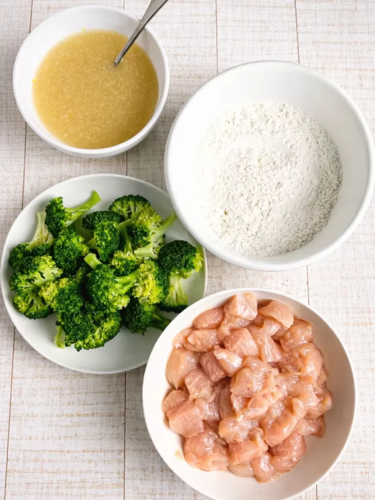 Ingredients for Crispy Lemon Honey Chicken laid out in bowls on white timber background.