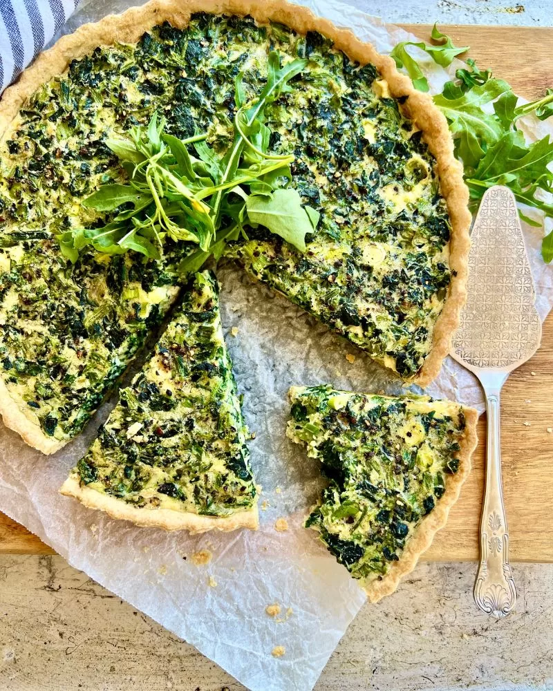 spinach and feta quiche with piece with a bite taken out. rocket leaves to garnish