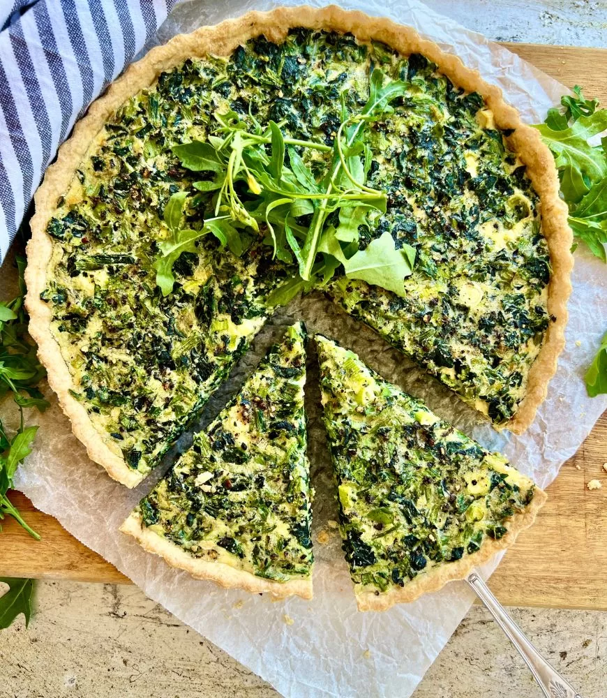 Spinach & feta quiche on baking paper with wedges cut out