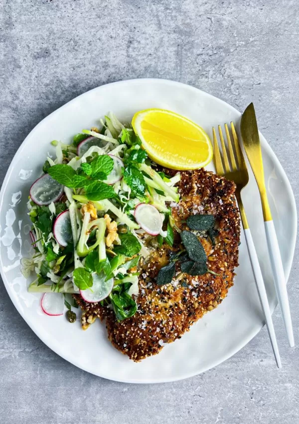 chicken schnitzel on white plate with salad, lemon cheek and cutlery