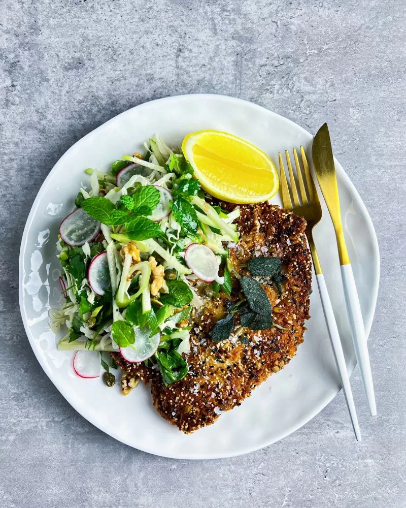 chicken schnitzel on white plate with salad, lemon cheek and cutlery