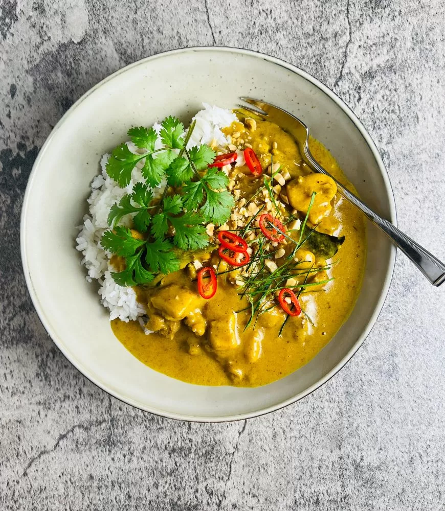 satay chicken curry in bowl with rice and garnishes on grey concrete background