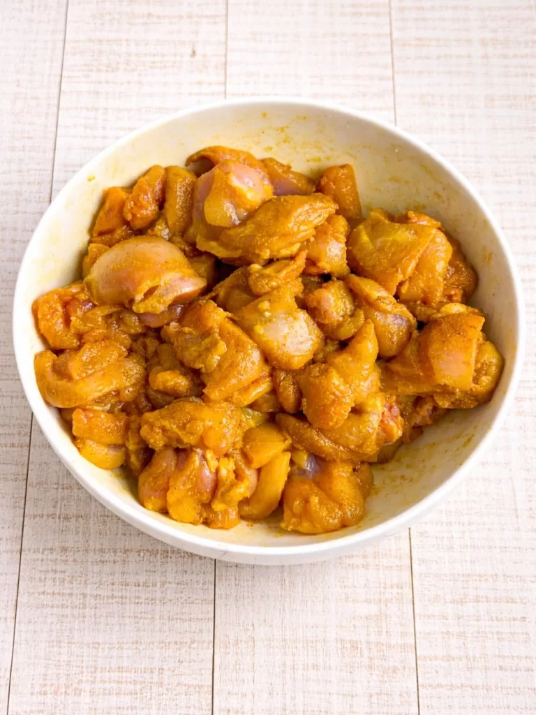 Chicken marinating in a white bowl on rustic white timber background.
