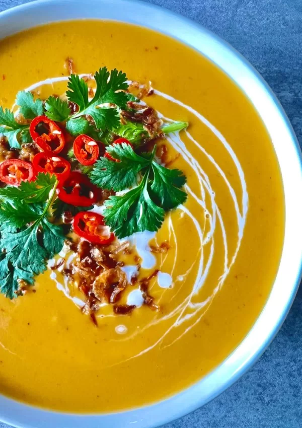 pumpkin soup in white bowl with coriander, chilli and fried shallots on top