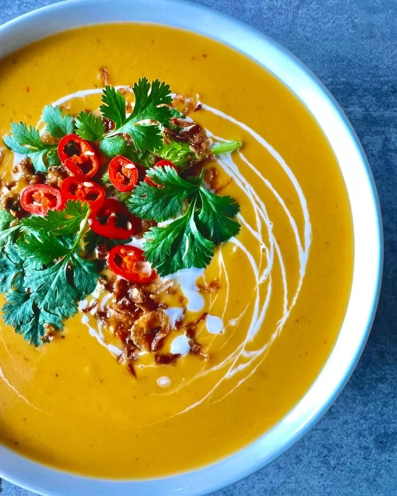 pumpkin soup in white bowl with coriander, chilli and fried shallots on top