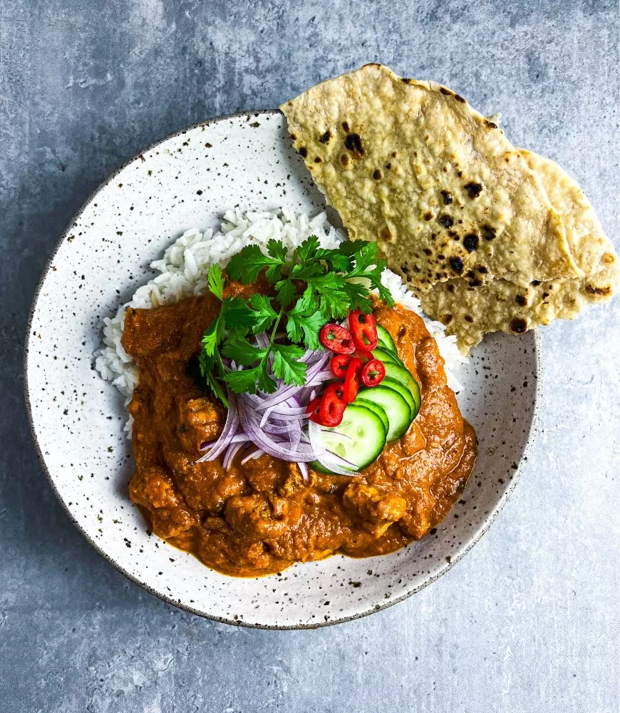 butter chicken in bowl with roti bread, rice and garnish