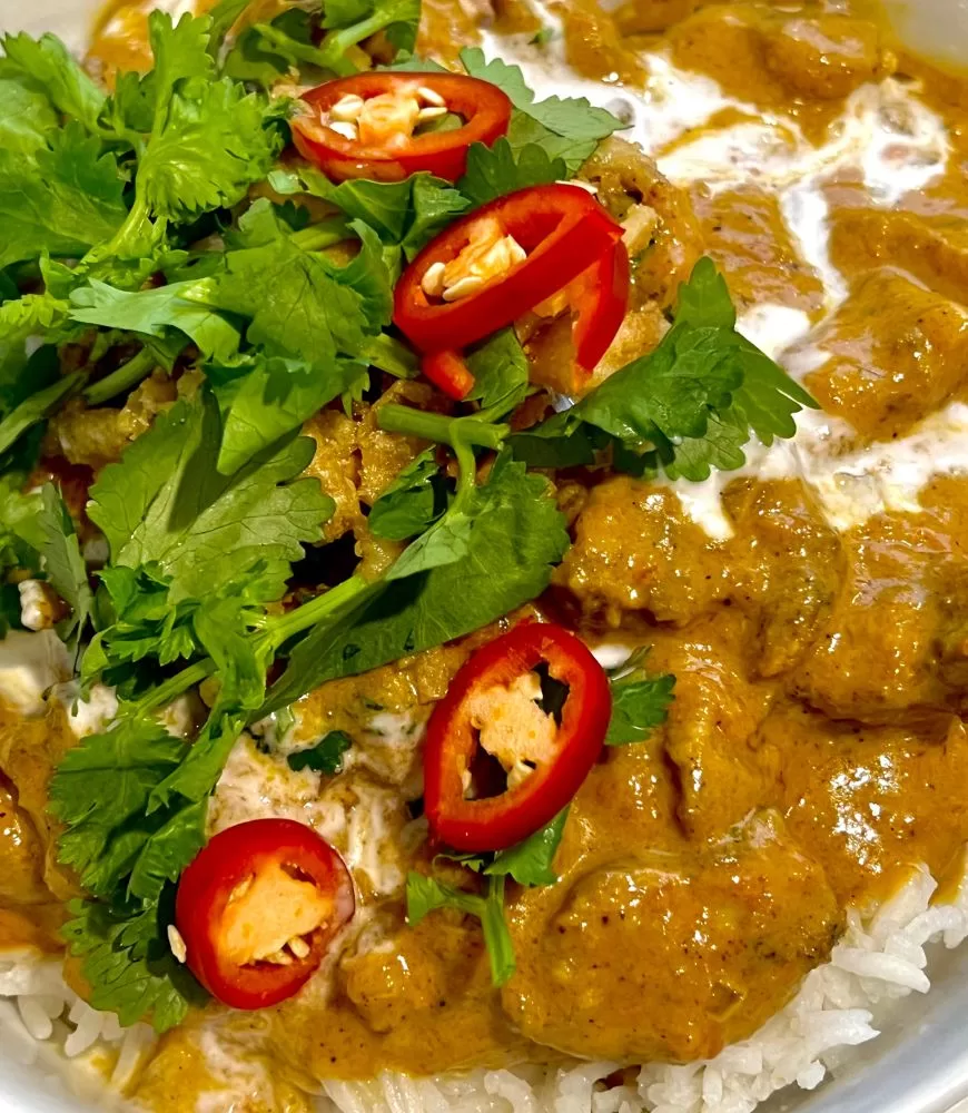 curry in a bowl over rice with sliced red chilli and chopped coriander on top