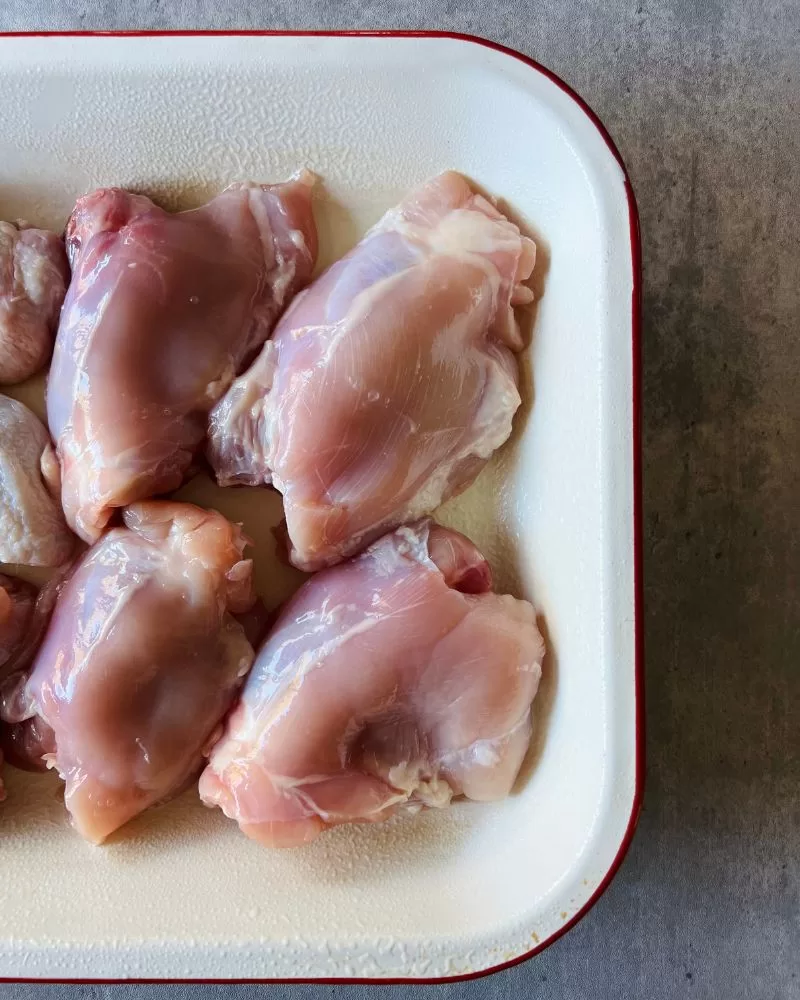 skinless chicken thigh cutlets in cream baking dish, grey background